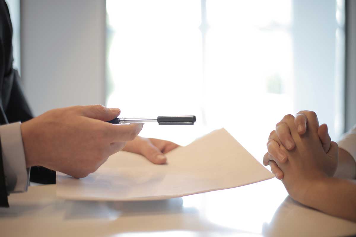 Business professional handing a pen and contract to an individual